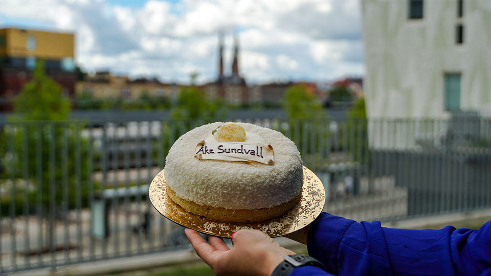 Två händer håller upp en tårta med texten Åke Sundvall. I bakgrunden syns Uppsala domkyrka.