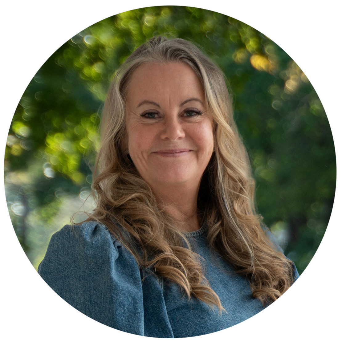Leende kvinna (Veronica) i blå topp i parkmiljö.