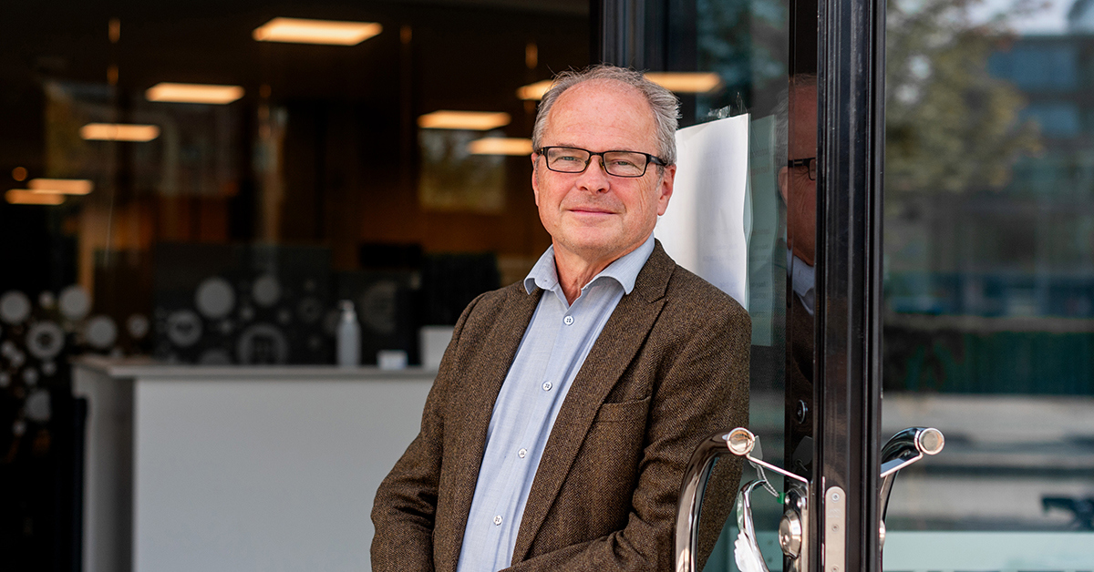 Leende man i kavaj står utanför kontor.